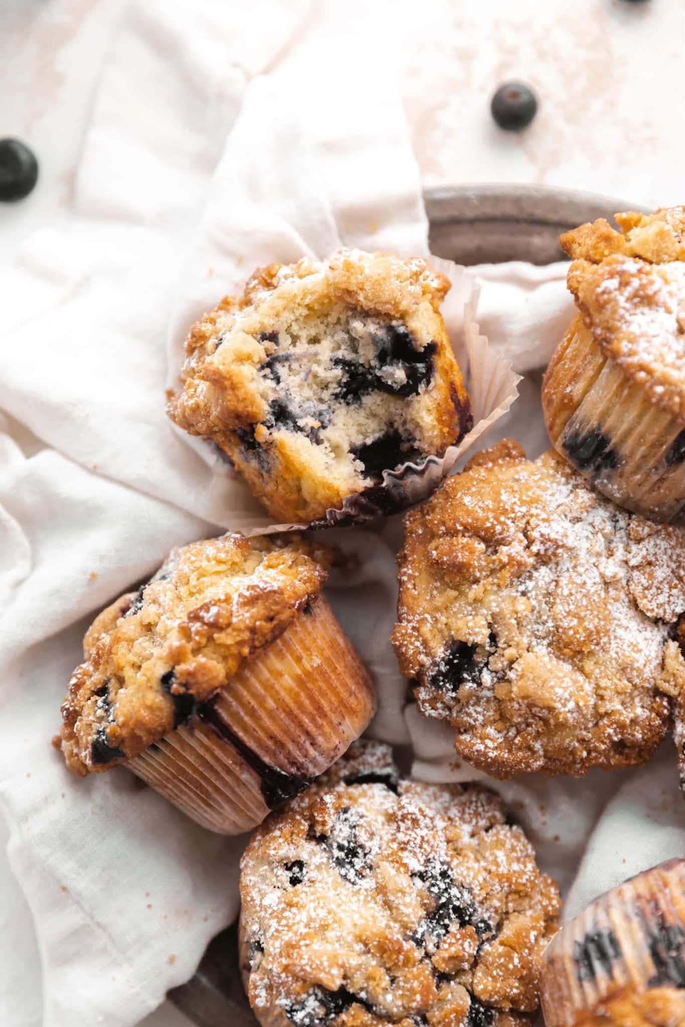Blueberry muffins dusted with powdered sugar on a white cloth.