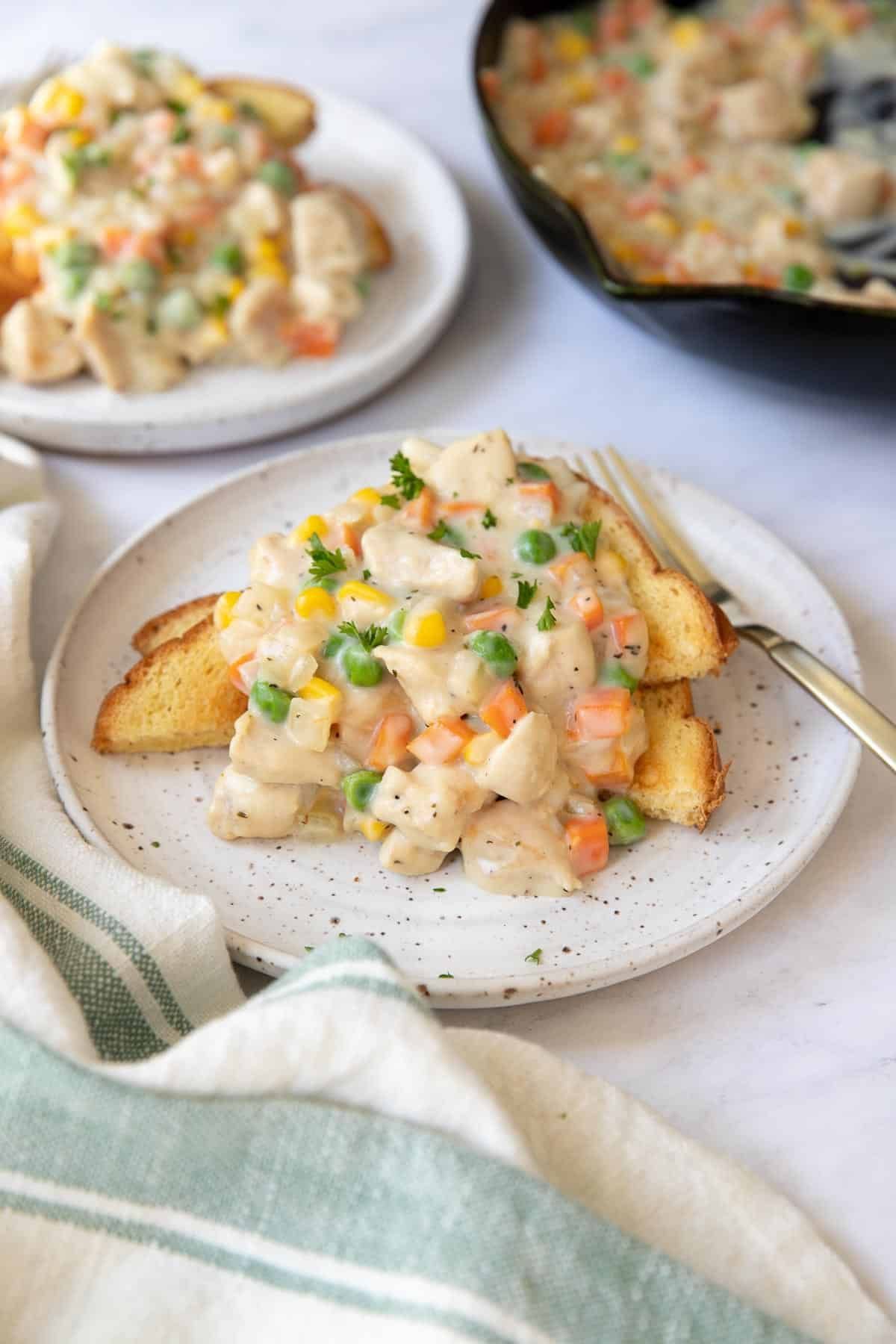 Creamy vegetable toast on a white plate with a fork, set on a striped cloth beside other plates