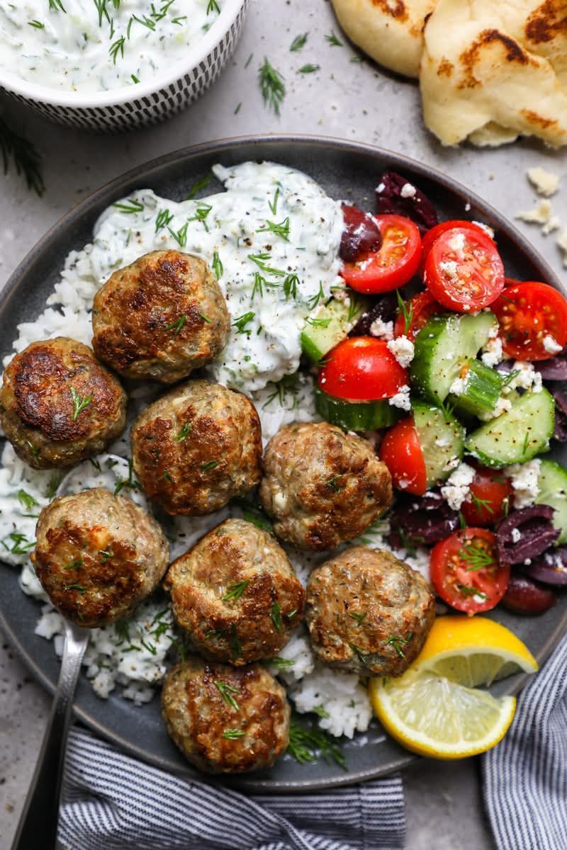 Falafel with rice, cucumber-tomato salad, tzatziki, and lemon wedges on a dark plate