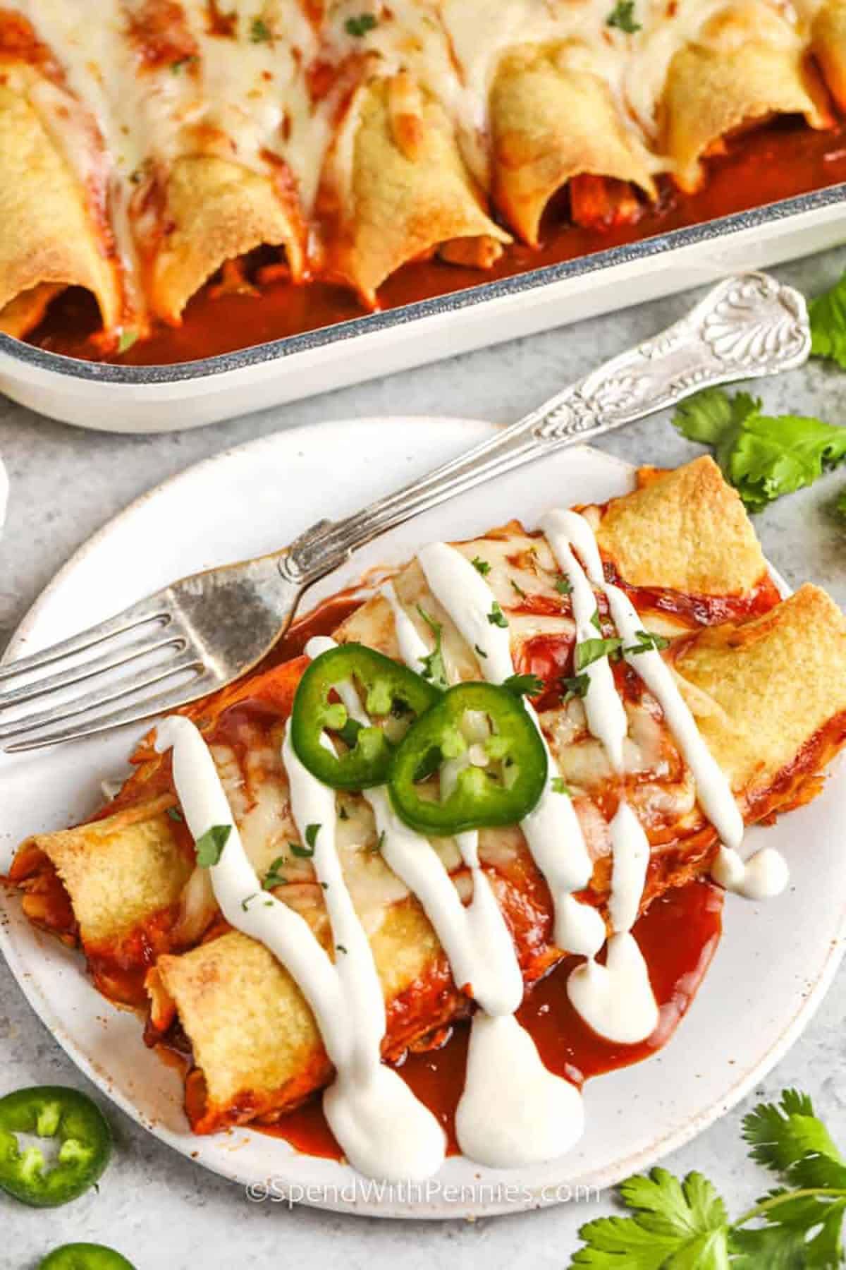 Cheesy baked enchiladas topped with salsa, sour cream, and jalapeños on a plate and baking dish