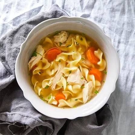 Bowl of chicken noodle soup with carrots, seen from above on a gray cloth