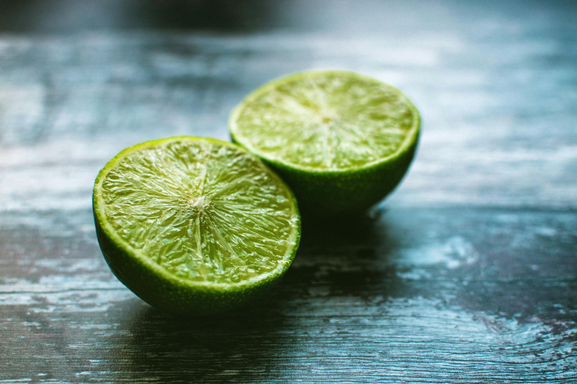 Two halved limes on a dark wooden surface with a blurred blue-green background