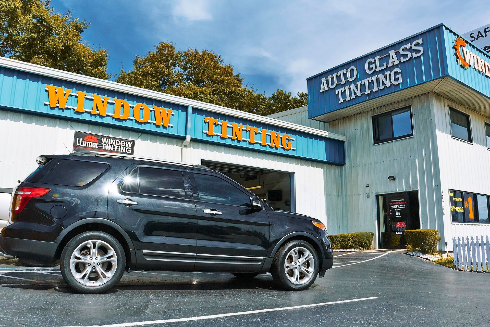 Black SUV parked in front of auto window tinting business with blue and orange signage.