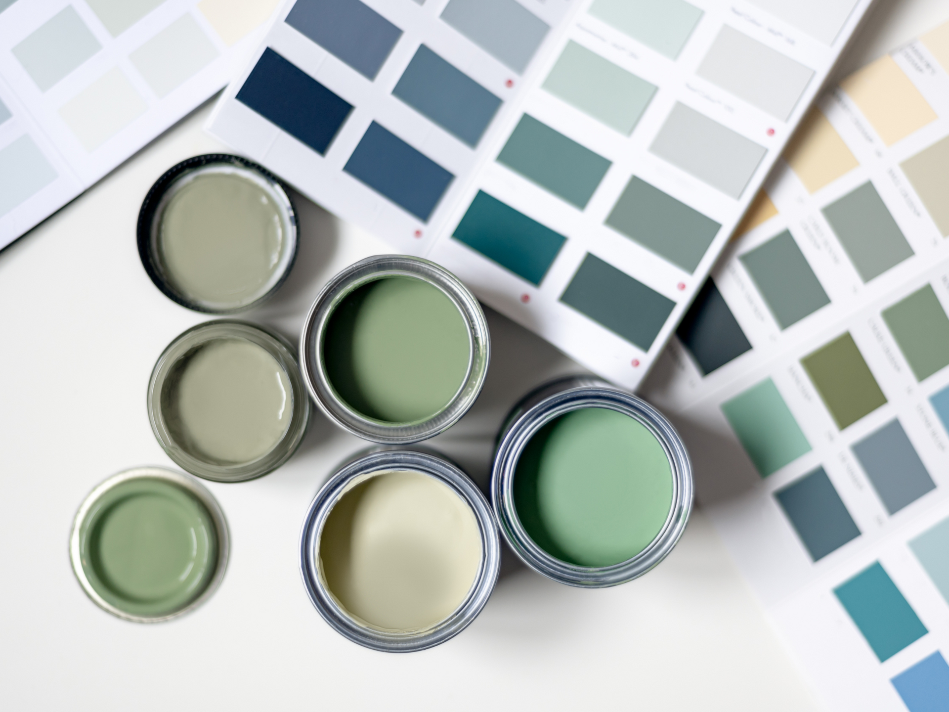 Paint sample tins open, displaying various shades of green, with corresponding color swatches on white surface.