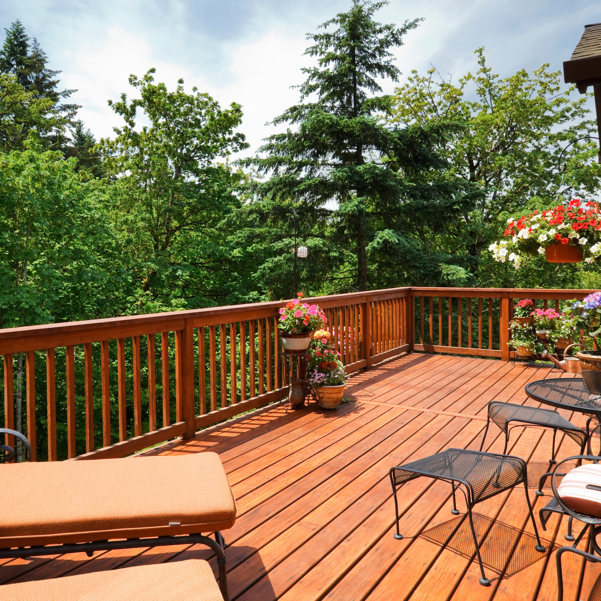 A stained wooden deck with chairs tables and flowers on it
