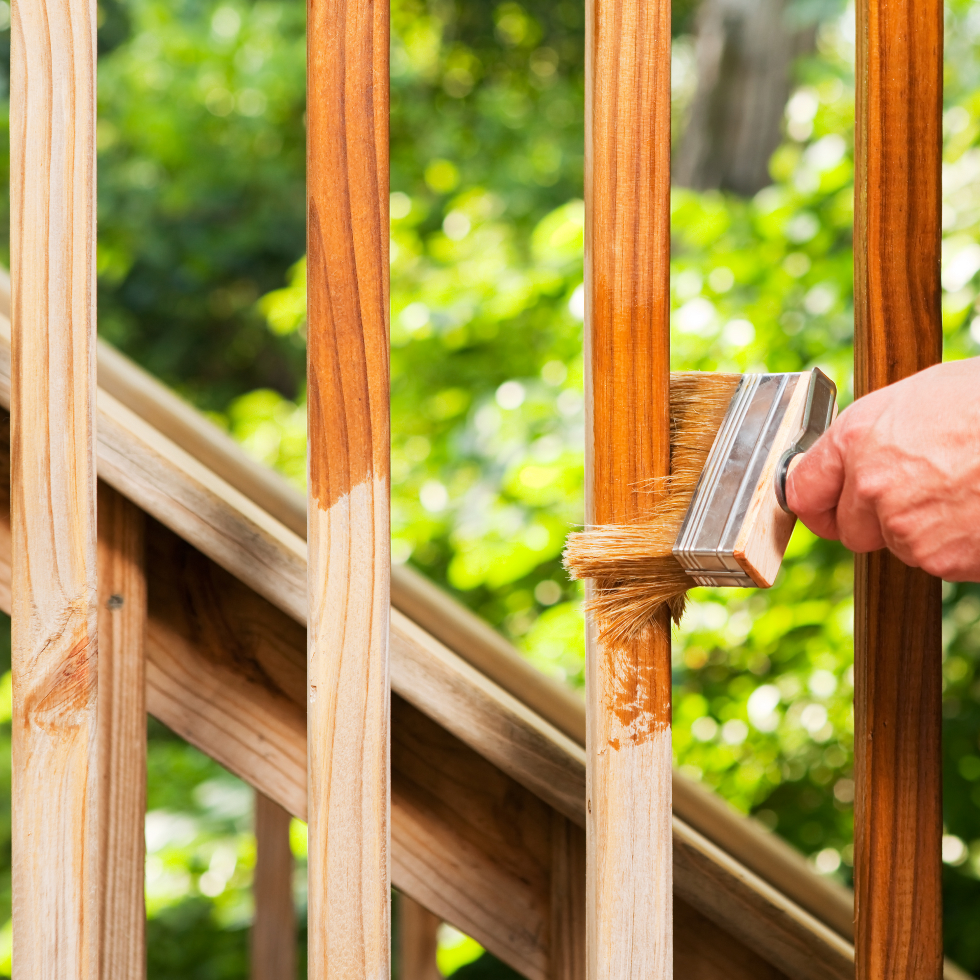 A person is staining a wooden railing with a brush