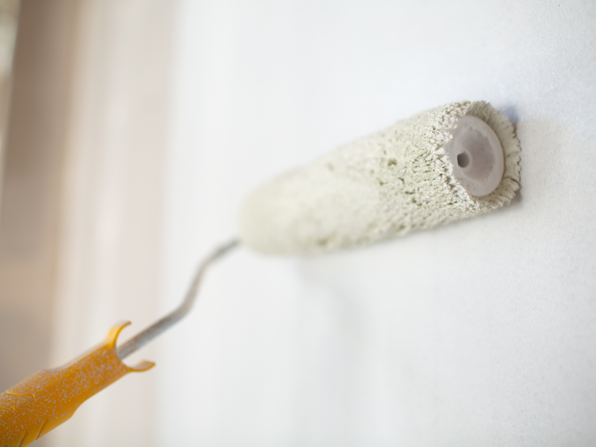A paint roller is being used to paint a white wall.