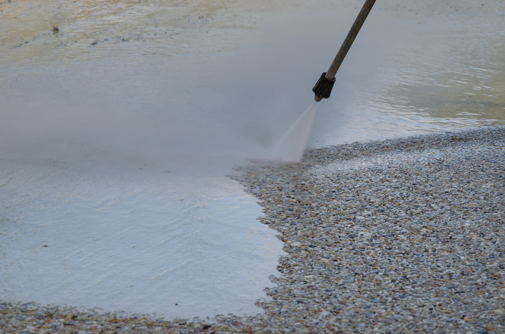 A person is using a high pressure washer to clean a gravel driveway.