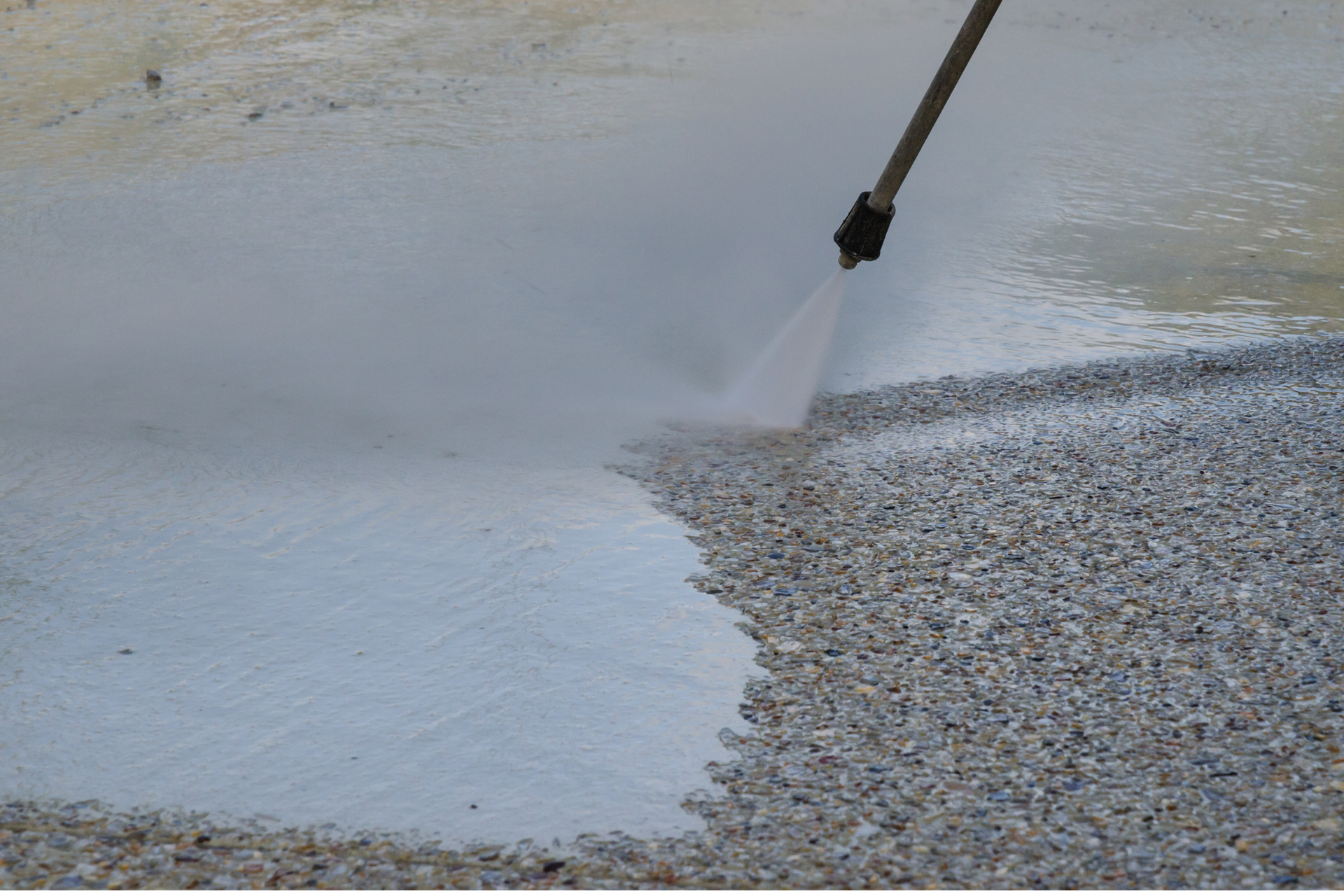 A person is using a high pressure washer to clean gravel