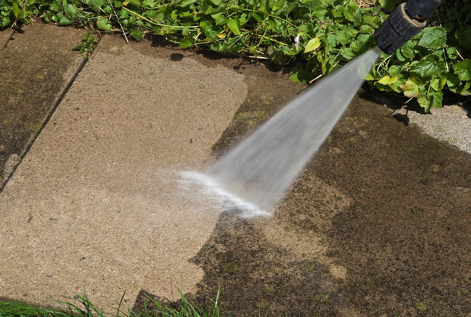 A person is using a high pressure washer to clean a sidewalk.
