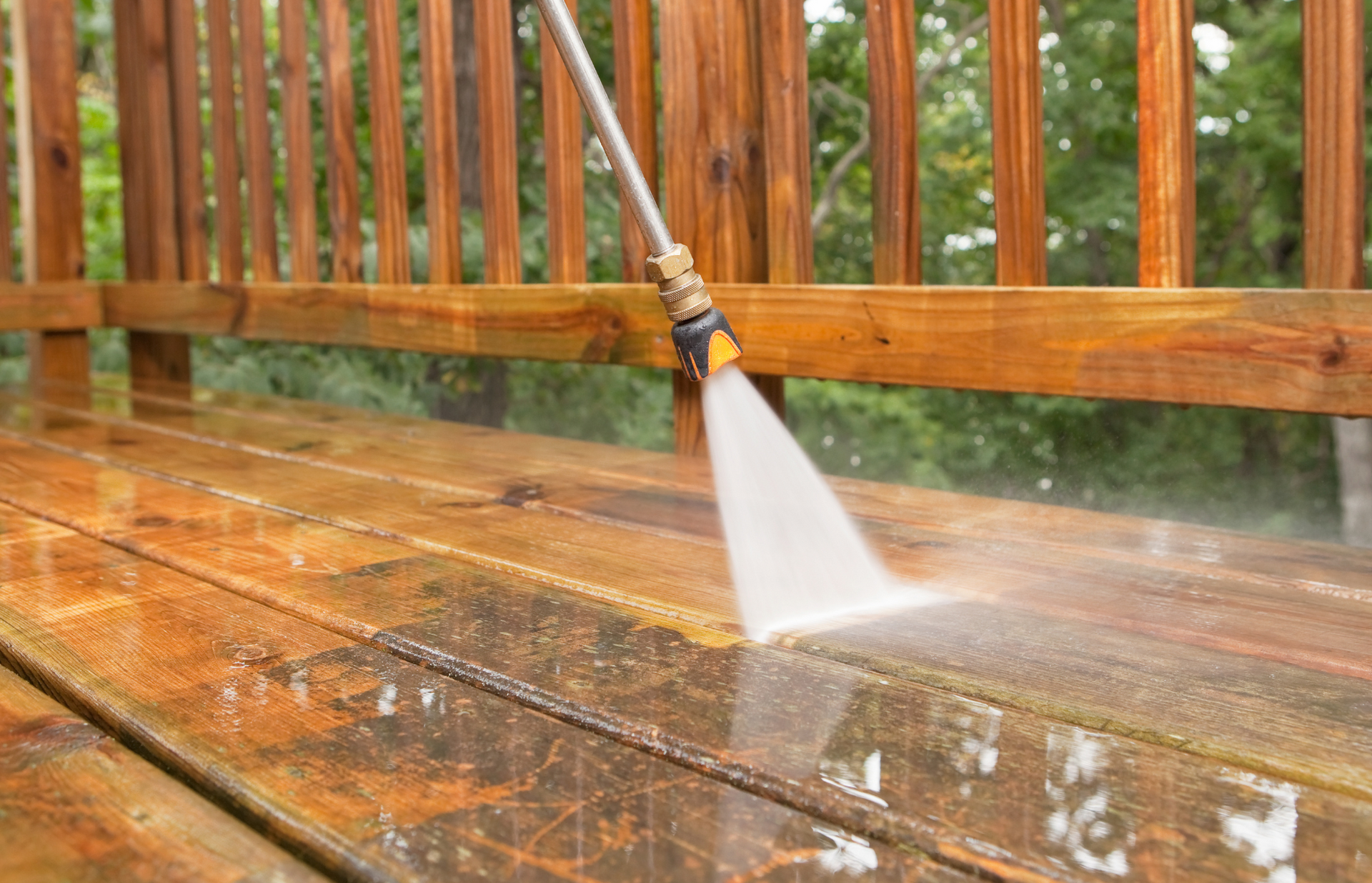 A person is using a high pressure washer to clean a wooden deck.