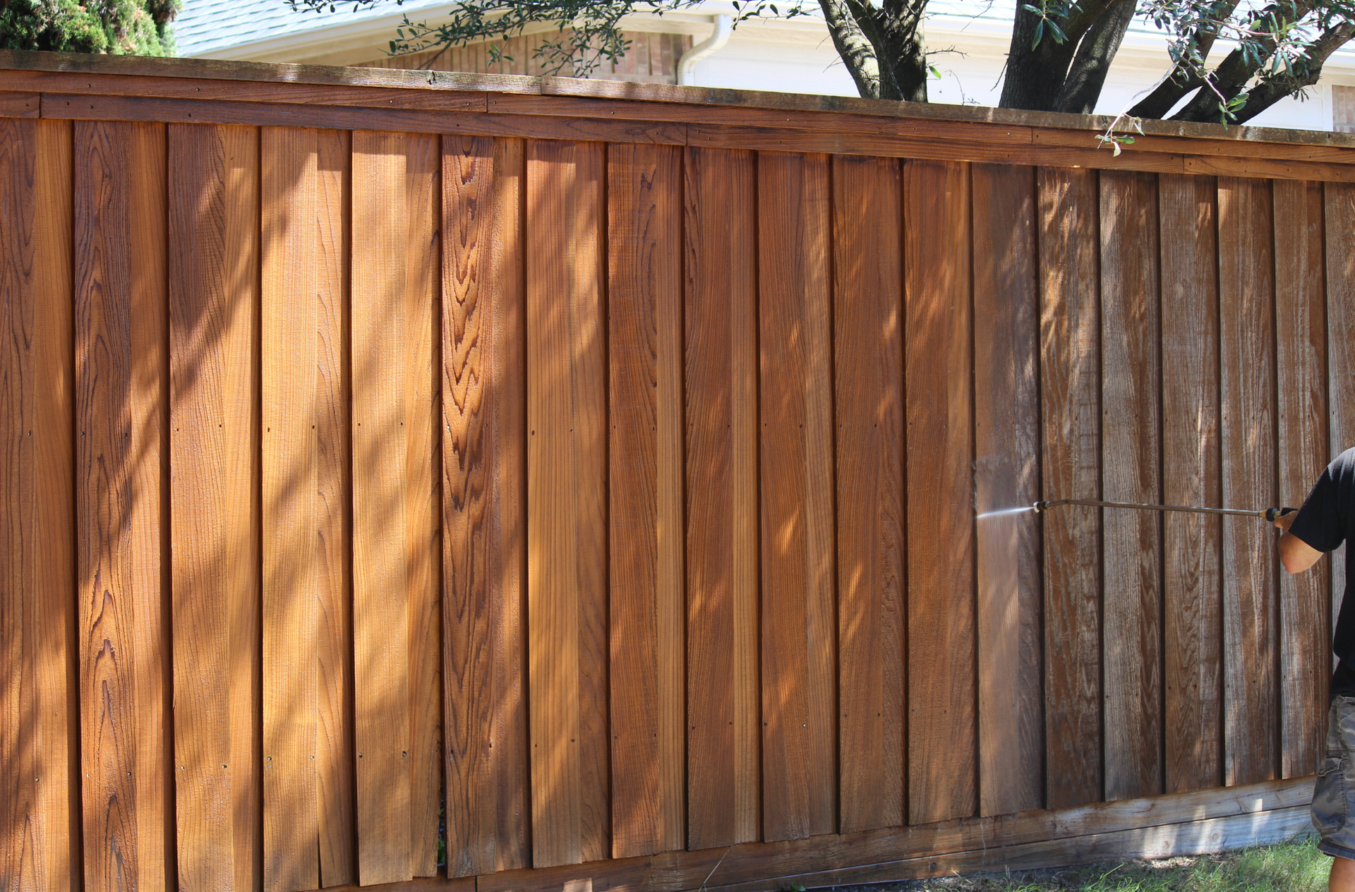 A man is power washing a wooden fence.