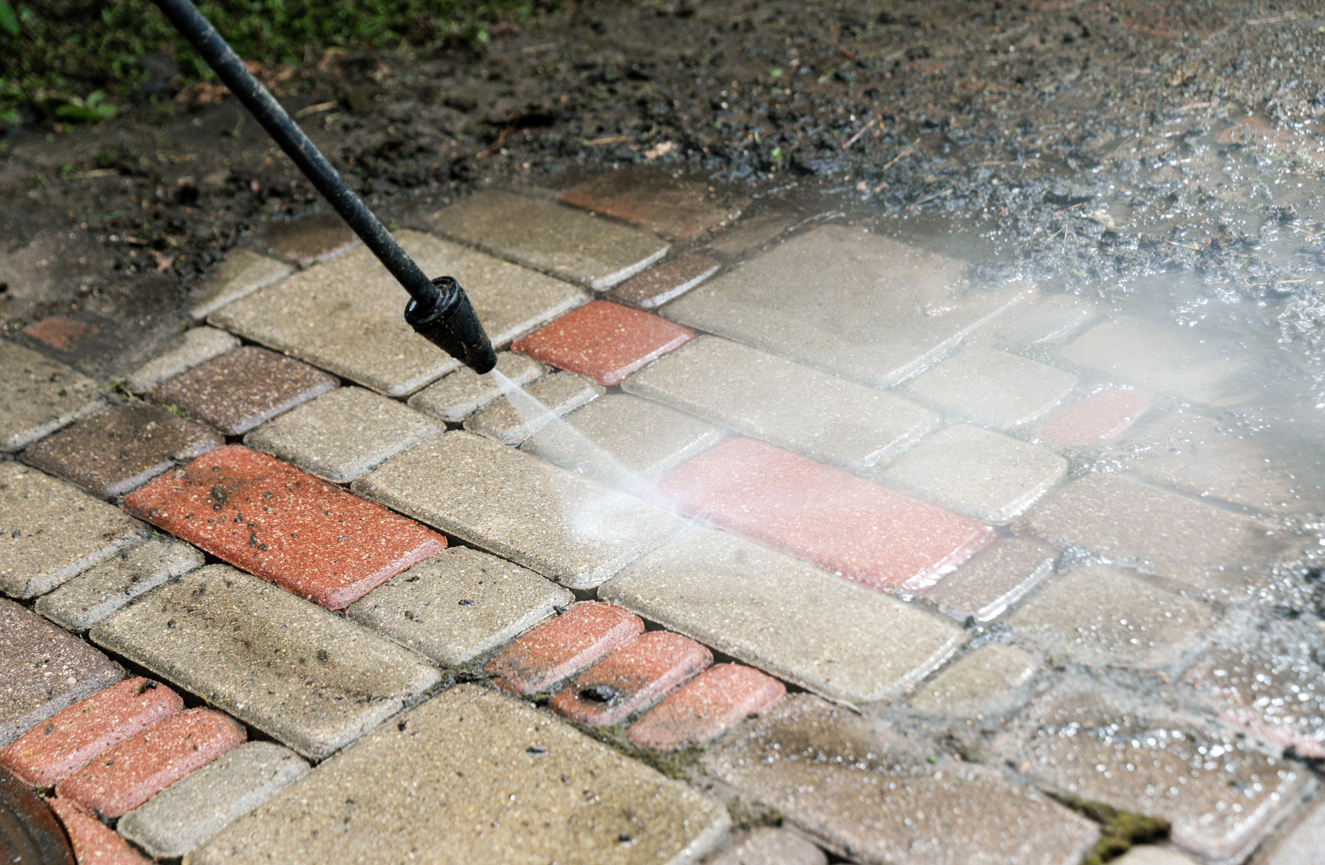 A person is using a high pressure washer to clean a brick walkway.