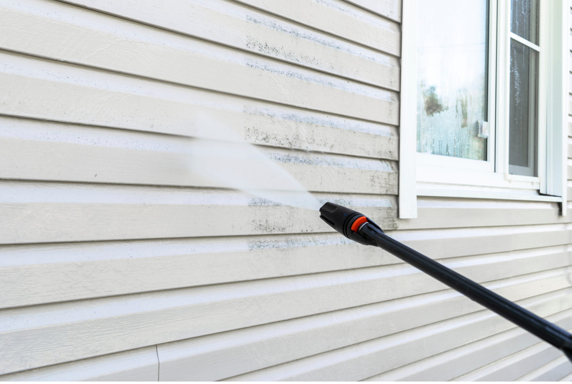 A person is using a high pressure washer to clean the side of a house.