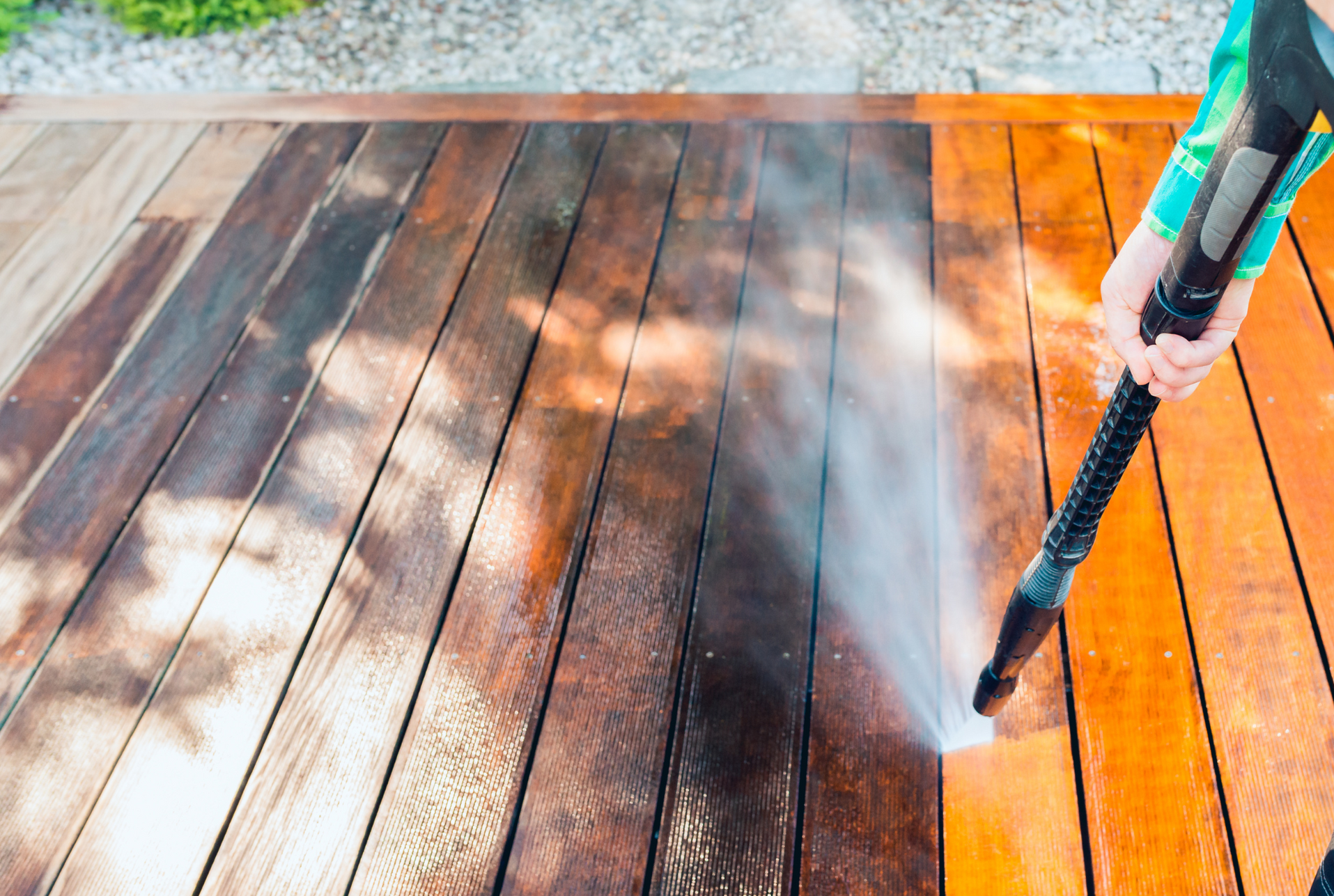 A person is cleaning a wooden deck with a high pressure washer.