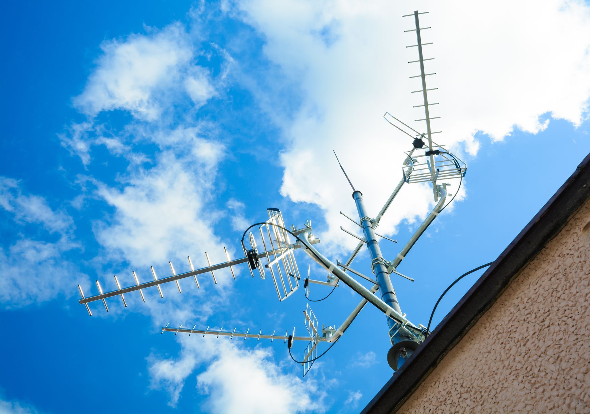 Television antenna on a rooftop against a bright blue sky with clouds. Television antenna on a rooftop against a bright blue sky with clouds.
