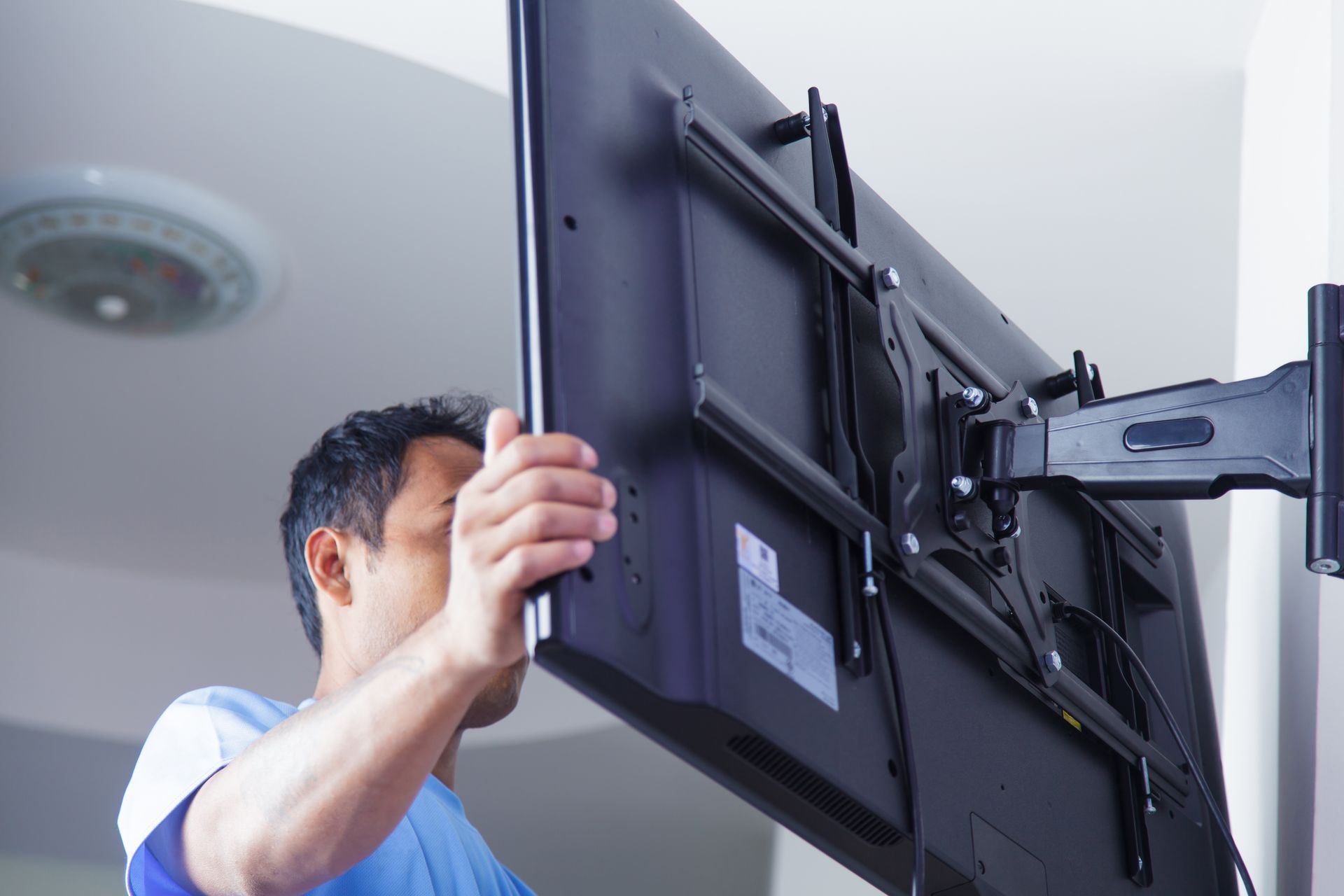 Person attaching a large flat-screen TV to a wall-mounted bracket. Person attaching a large flat-screen TV to a wall-mounted bracket.