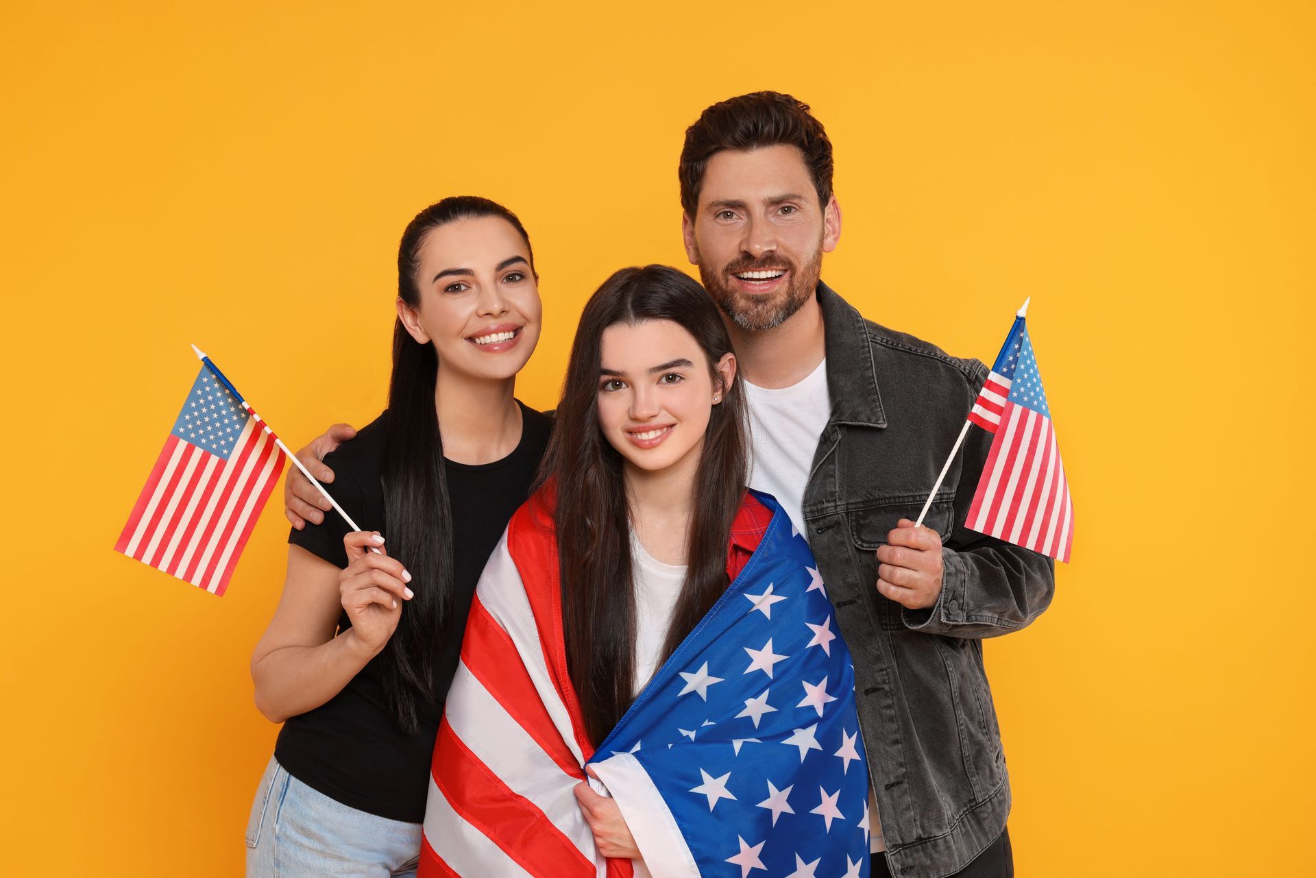 Three people holding U.S. flags against a bright yellow background