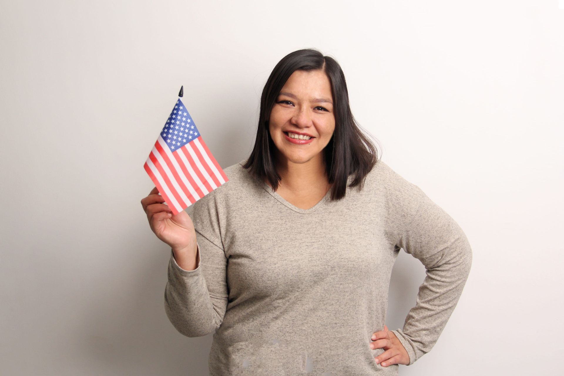 Woman holding a small American flag and smiling against a plain background