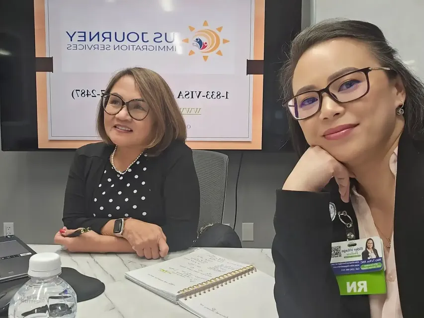 Two women seated at a conference table in front of a SUNJUNNY sign, one smiling at the camera.