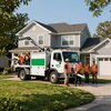 Utility workers in orange vests beside a white bucket truck in front of a suburban house Utility workers in orange vests beside a white bucket truck in front of a suburban house