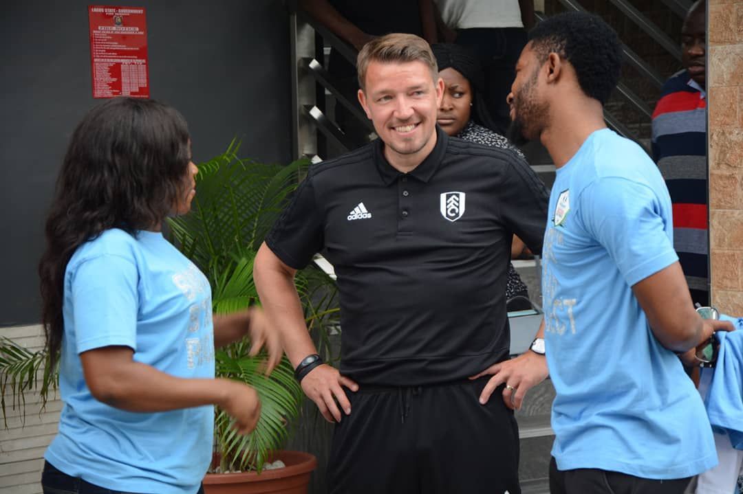 Three people in sportswear smiling and talking outdoors near a building