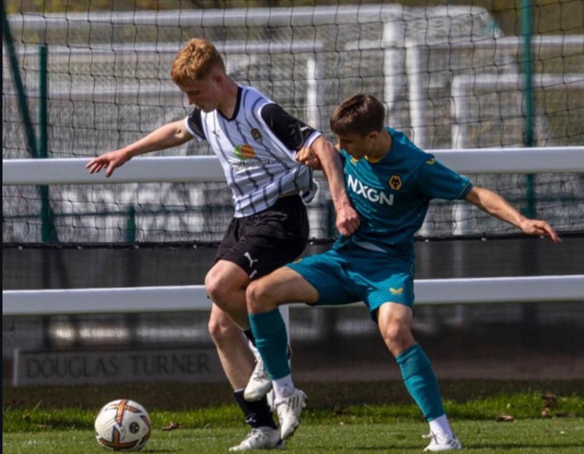 Two soccer players in white and teal battling for the ball on a field.