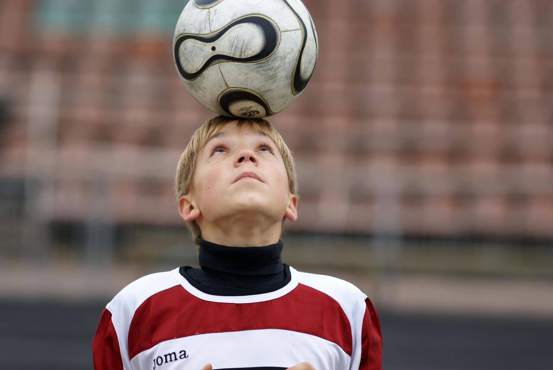 Soccer player balancing a ball on his forehead during practice, wearing a red-and-white jersey