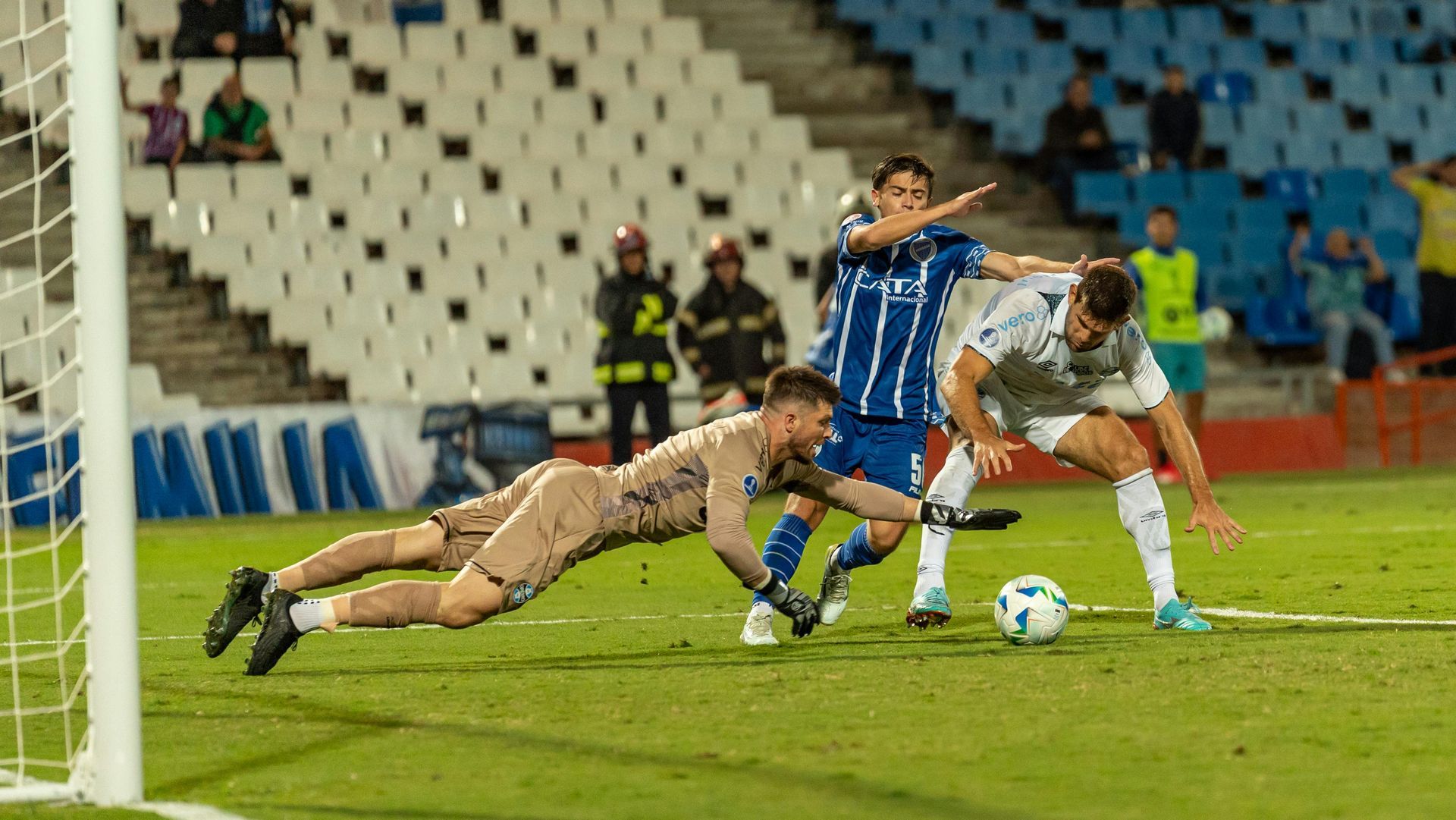 Packed soccer stadium at night with players on a bright green field and crowded stands