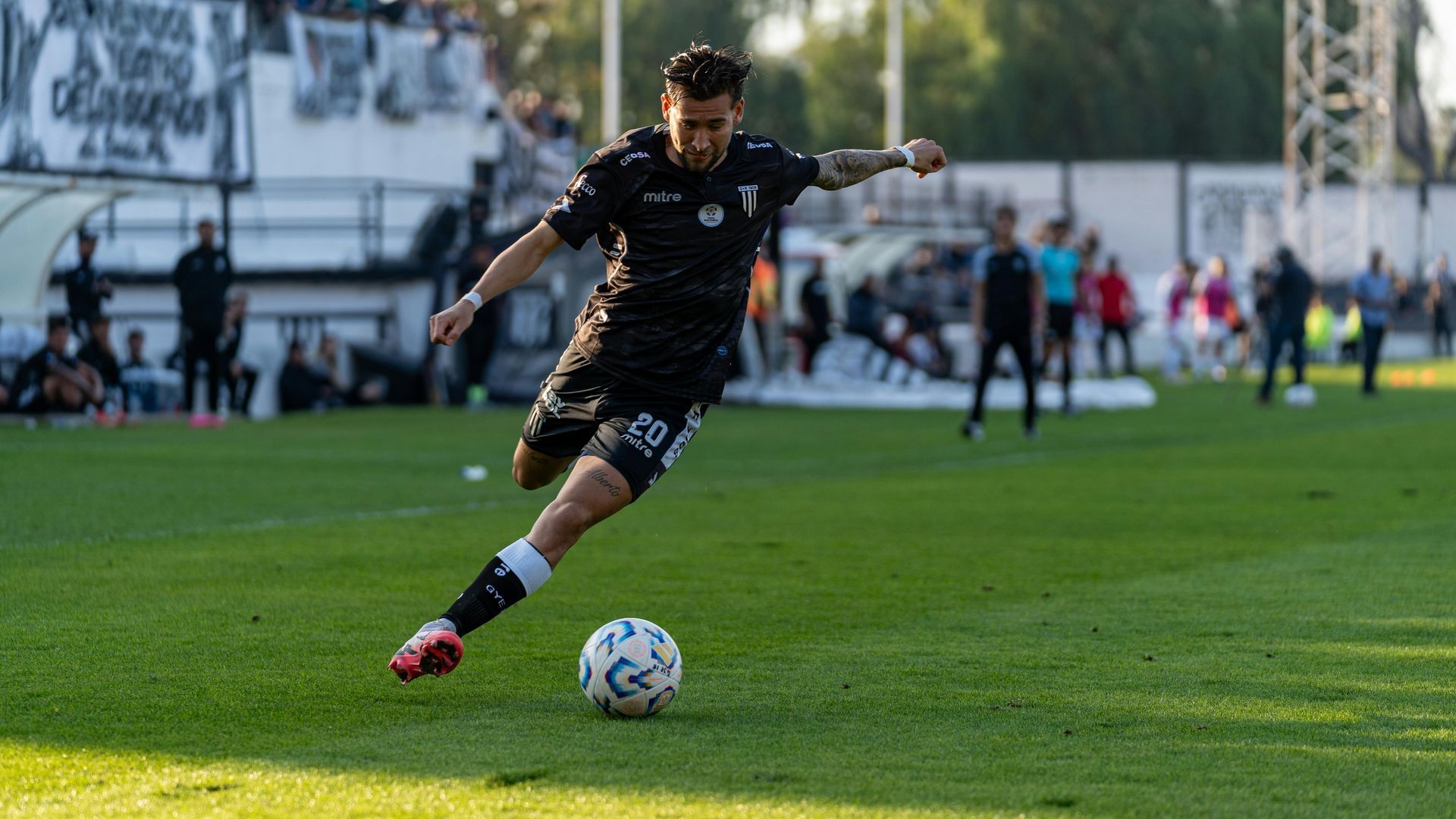 Soccer player in black uniform kicks a ball on a grassy field during a match