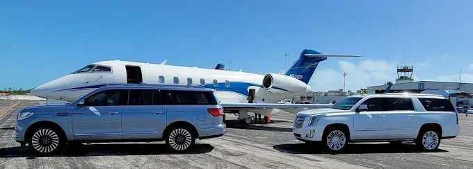 Two SUVs parked on a tarmac in front of a private jet at an airport on a clear day.