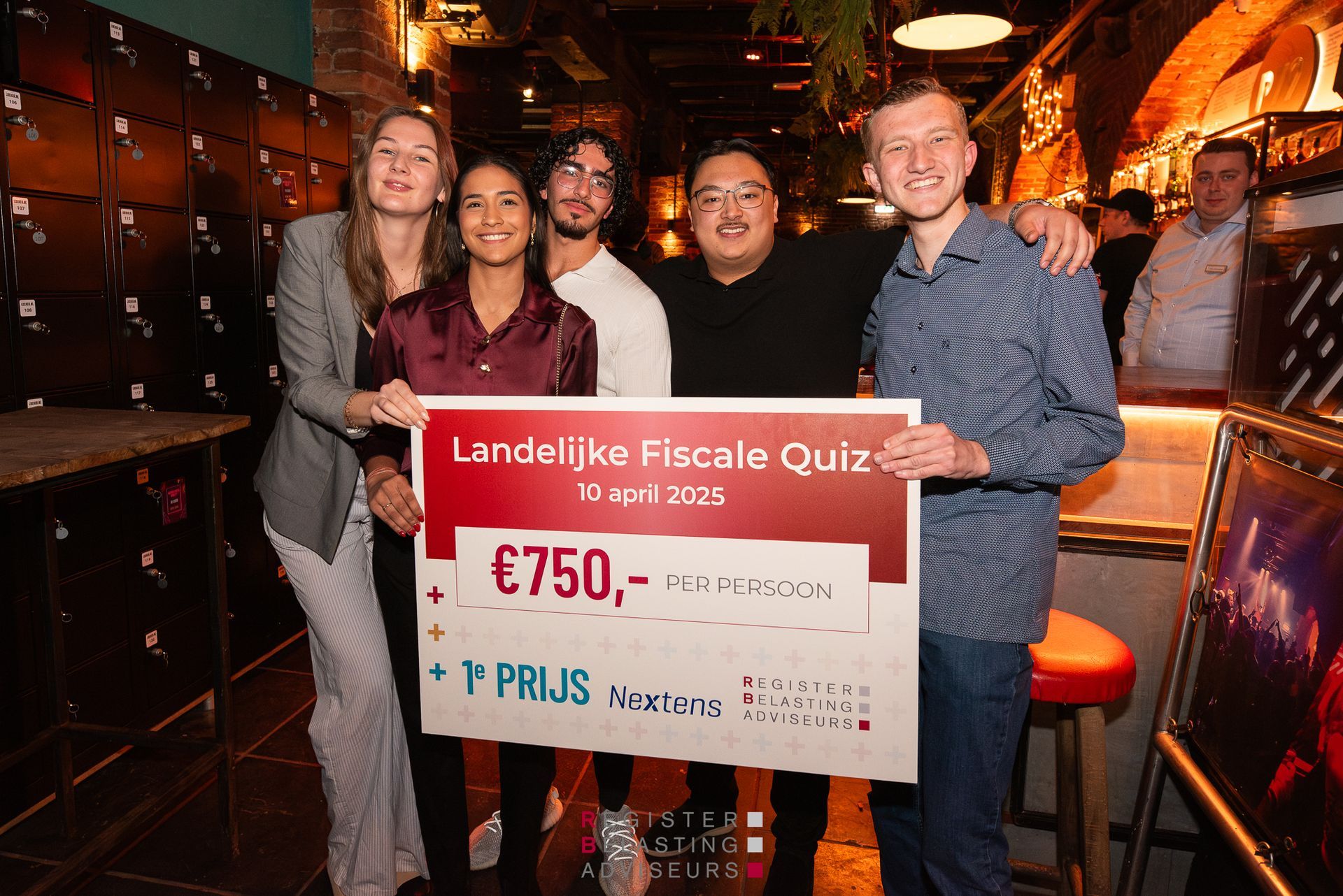 Vier mensen poseren binnen met een grote cheque ter waarde van €750 tijdens een Landelijke Pub-Quiz evenement.