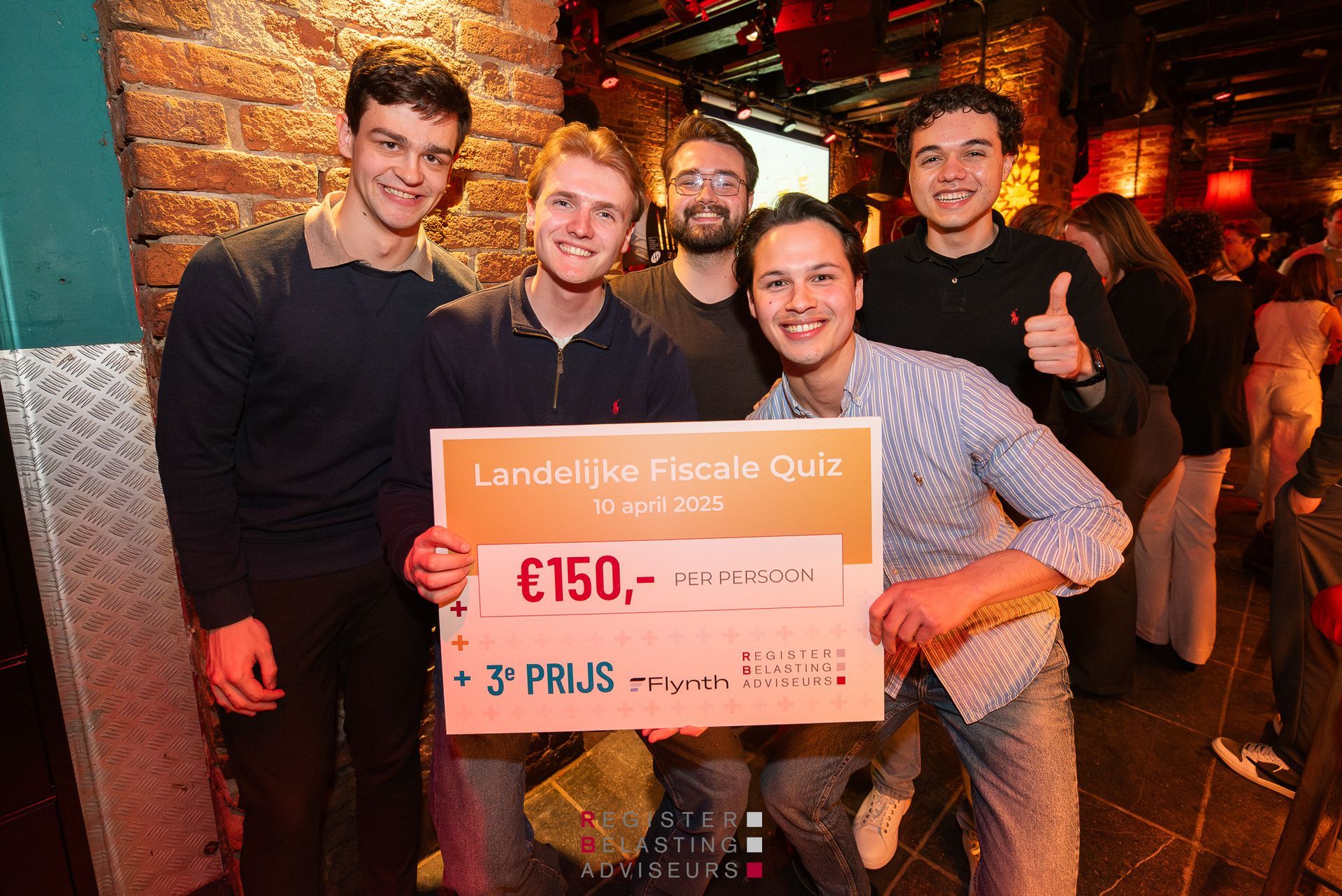 Vijf mensen in een bar houden een grote roze prijzencheque vast en lachen naar de camera.
