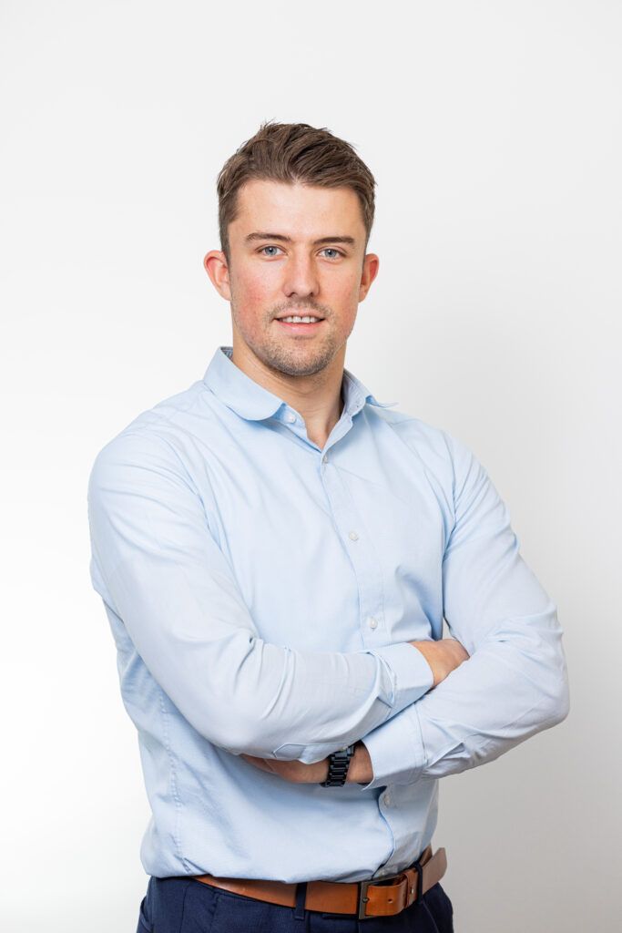 Man in een lichtblauw overhemd staat met gekruiste armen tegen een witte achtergrond.