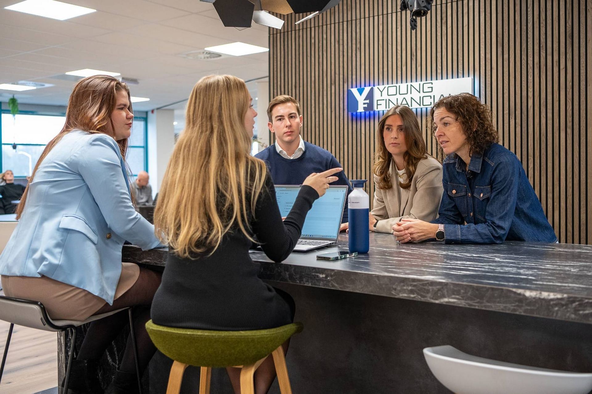Een groep mensen vergadert op een financieel kantoor en overlegt via een laptop.