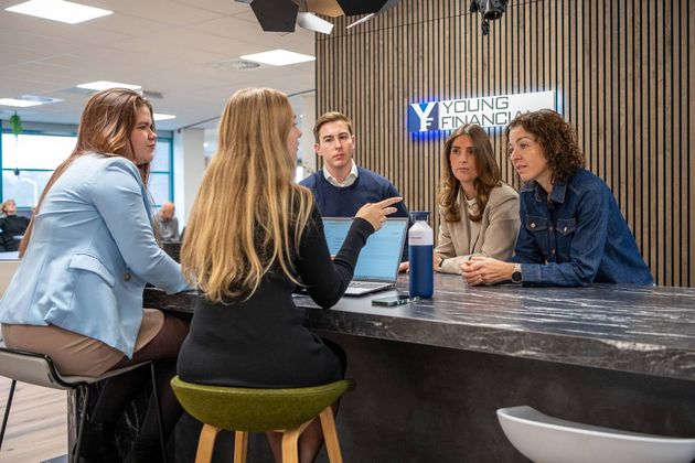 Een groep mensen vergadert op een financieel kantoor en overlegt via een laptop.