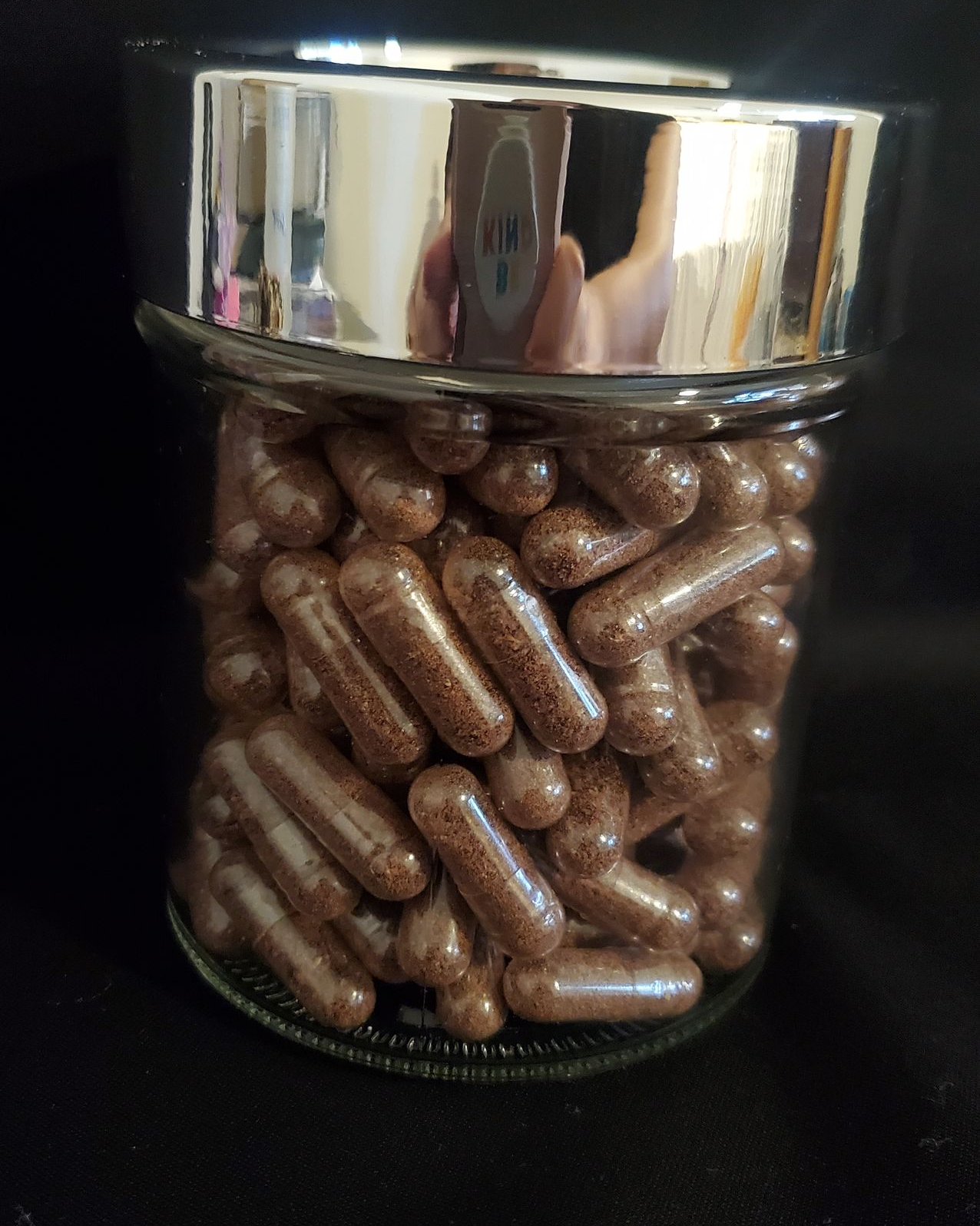 Brown capsules in a glass jar with a silver lid, resting on a black surface.