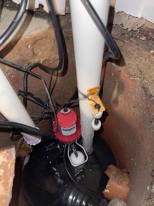 Sump pump in a pit with red motor, white pipe, and black tubing.