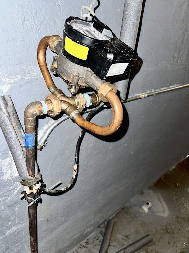 Water meter with copper pipes attached to a gray wall.