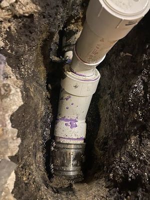 White PVC pipes connected in a dark trench. A metal fitting joins the PVC.