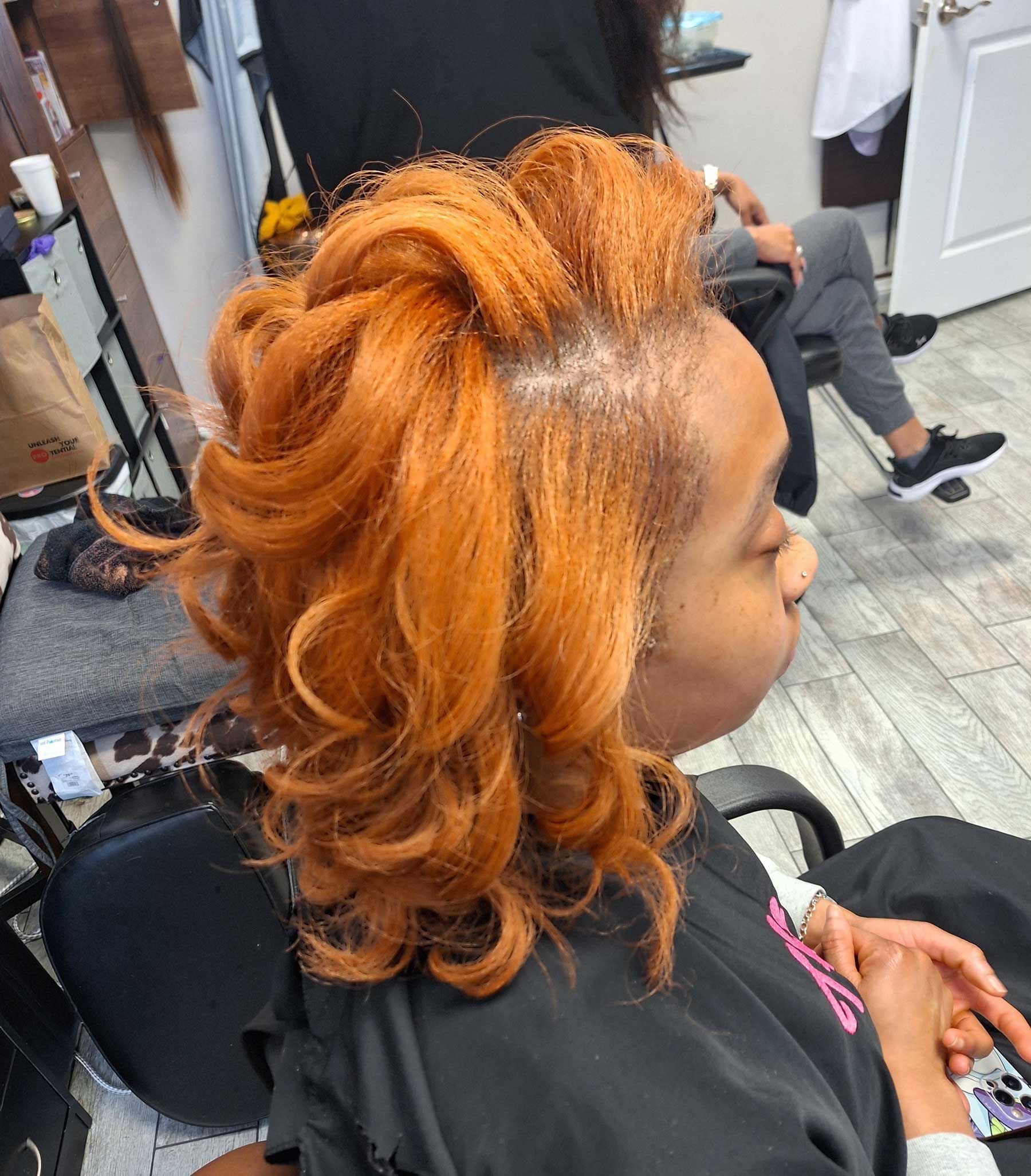 A woman with orange hair is sitting in a chair in a salon.