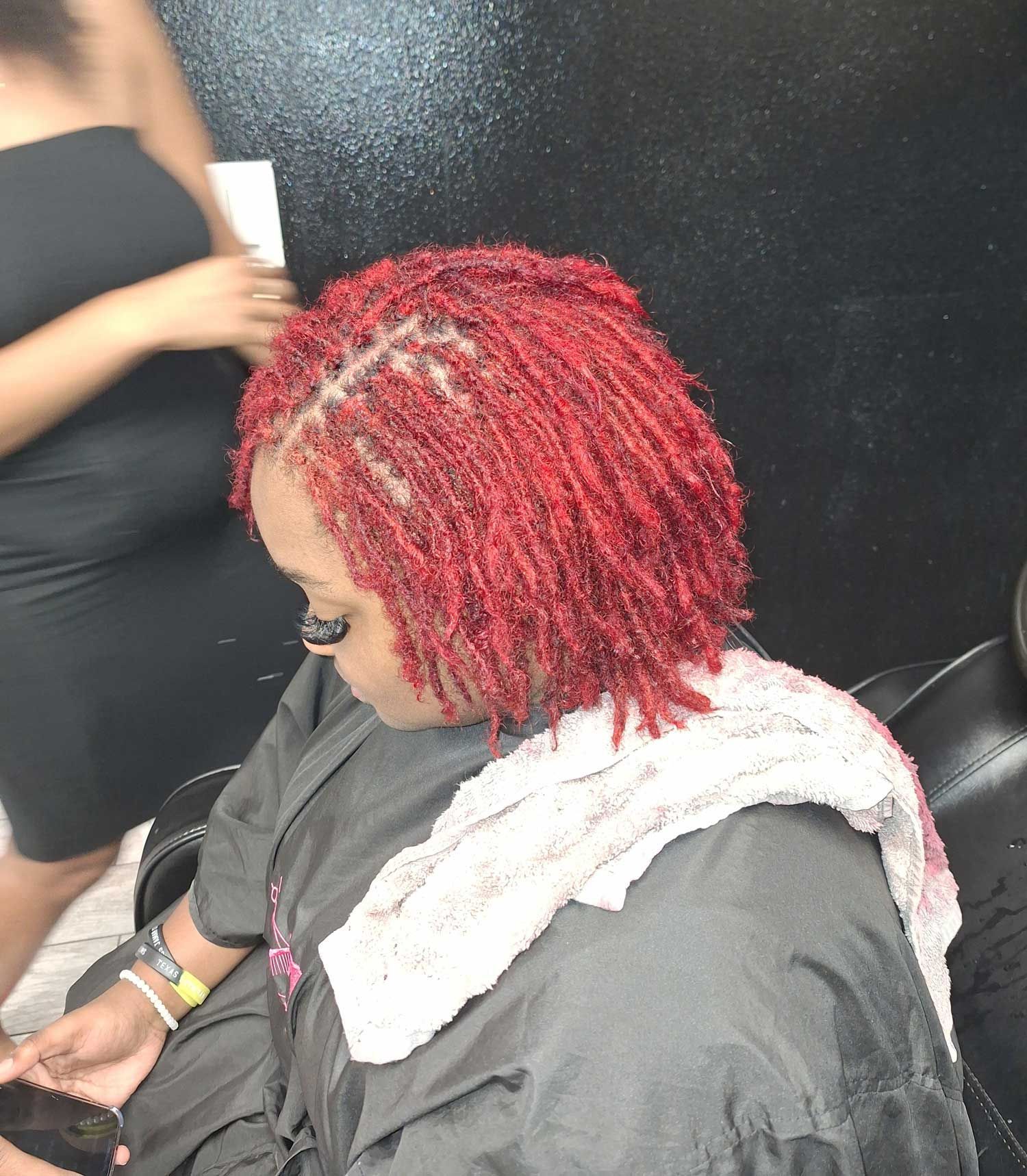 A woman with red hair is sitting in a chair with a towel around her neck.