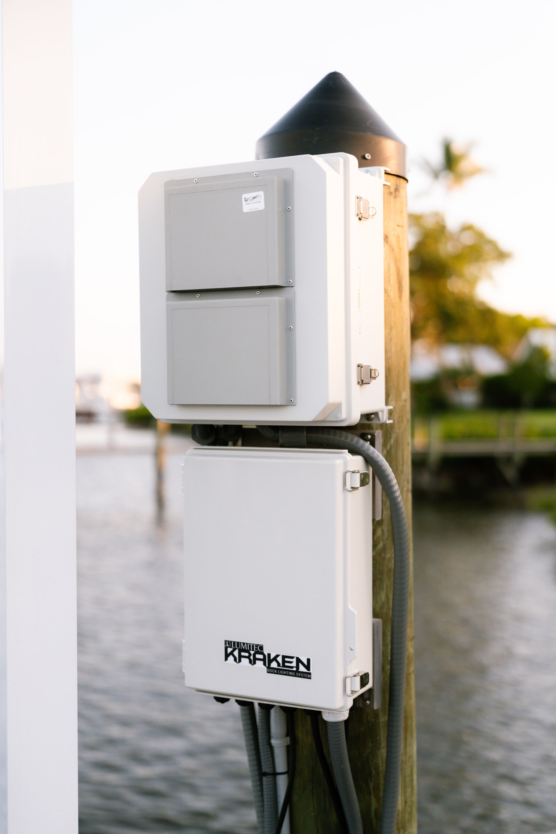 A white box is sitting on top of a wooden post next to a body of water.