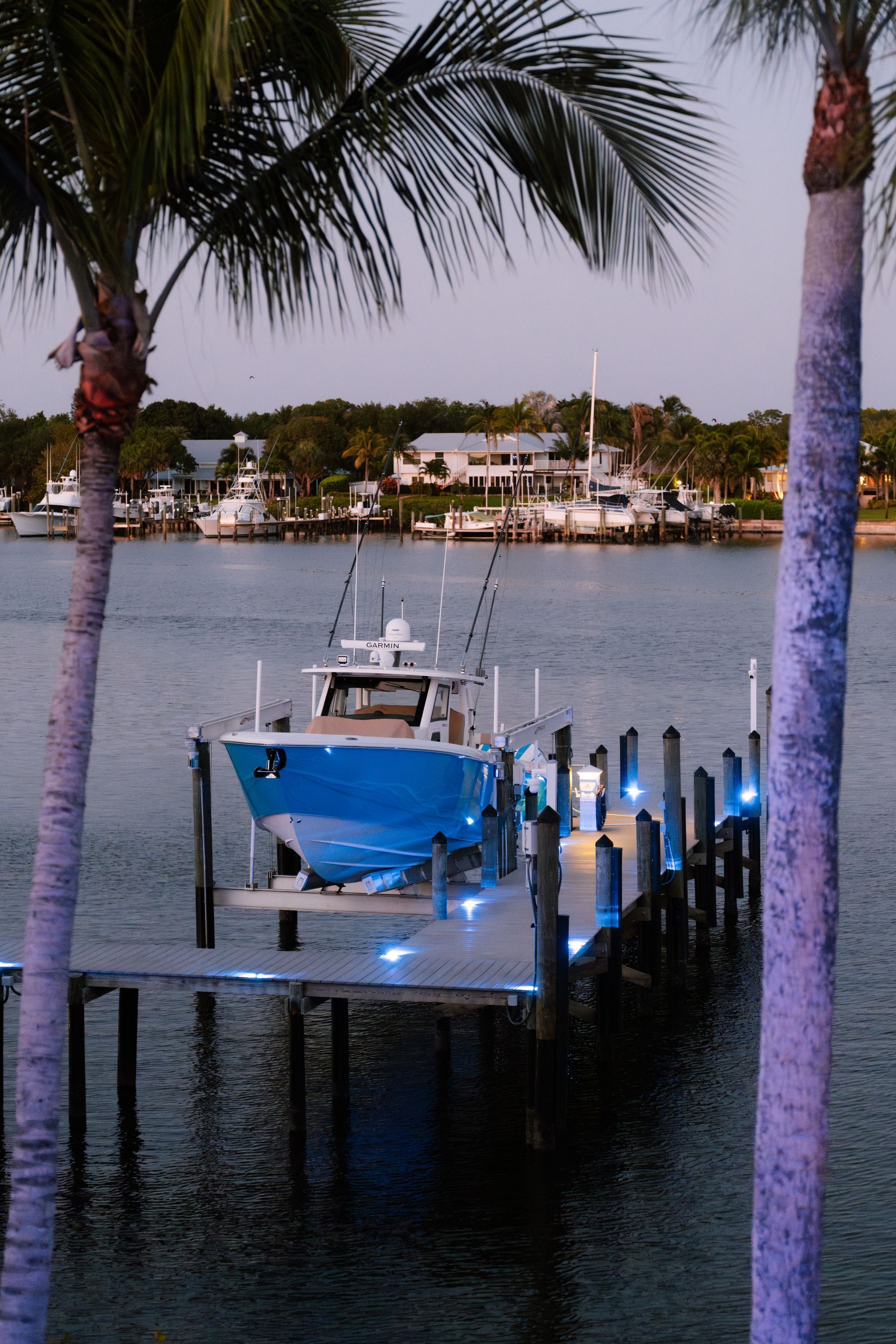 A blue boat is docked at a dock surrounded by palm trees