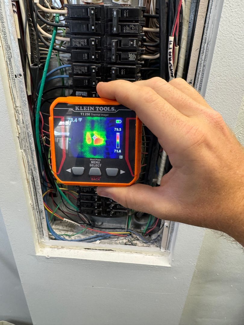 A person is holding a thermal imager over an electrical panel.