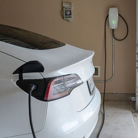 A white car is plugged into a charging station in a garage.