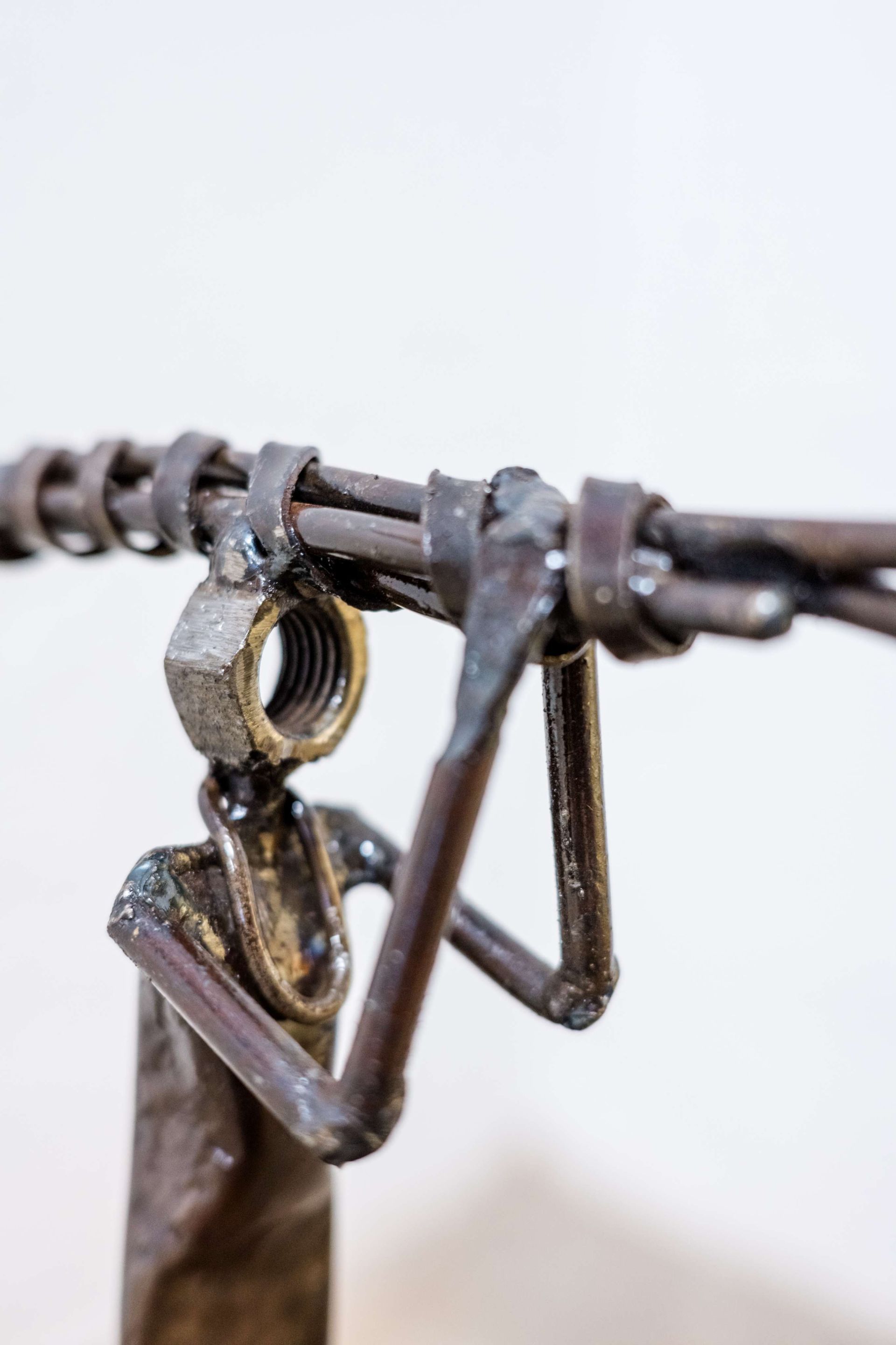Lady Carrying Wood scrap metal sculpture by Pilato Bulala showing figure carrying firewood on wooden base against white wall