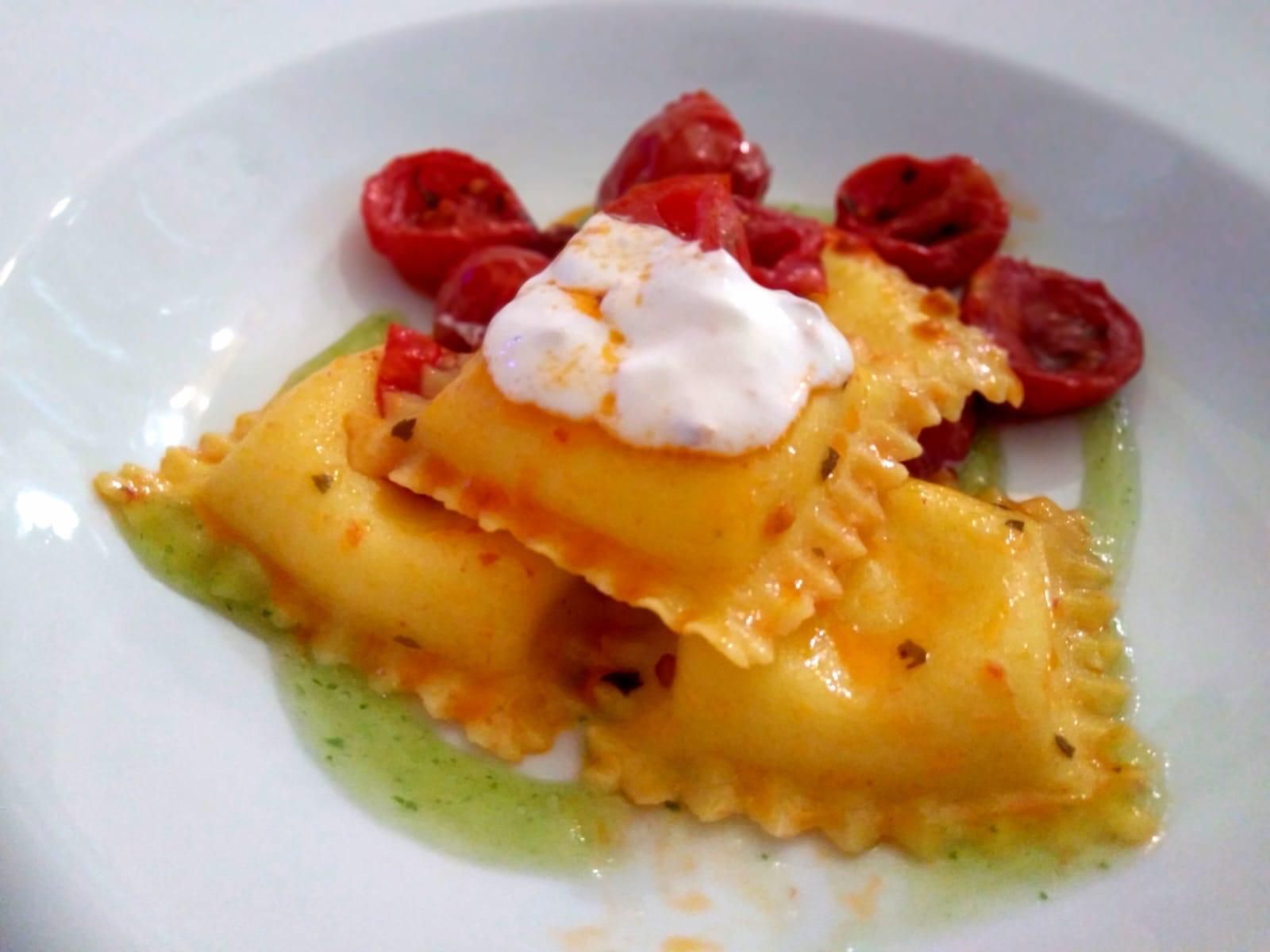 Ravioli impiattati con panna, guarniti con pomodorini tagliati a metà e salsa verde.