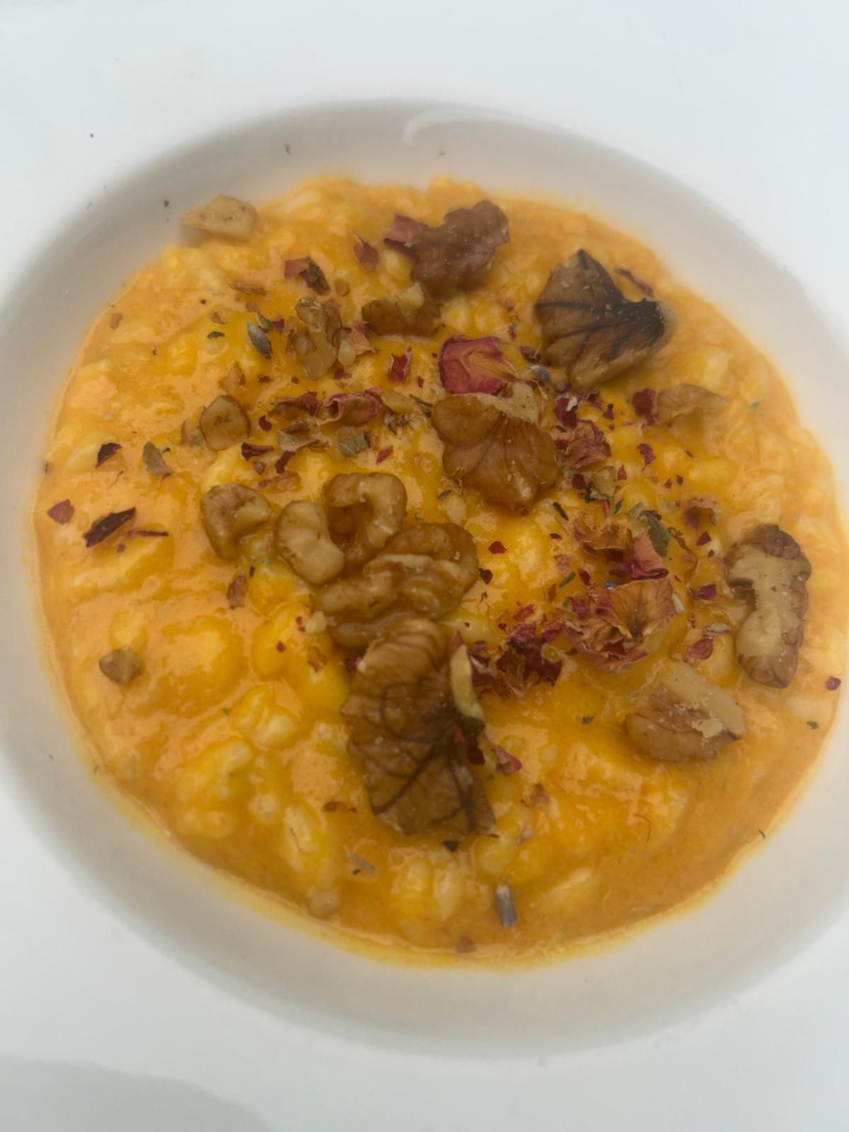 Zuppa cremosa all'arancia guarnita con pezzi di noci e peperoncino in scaglie, servita in una ciotola bianca.
