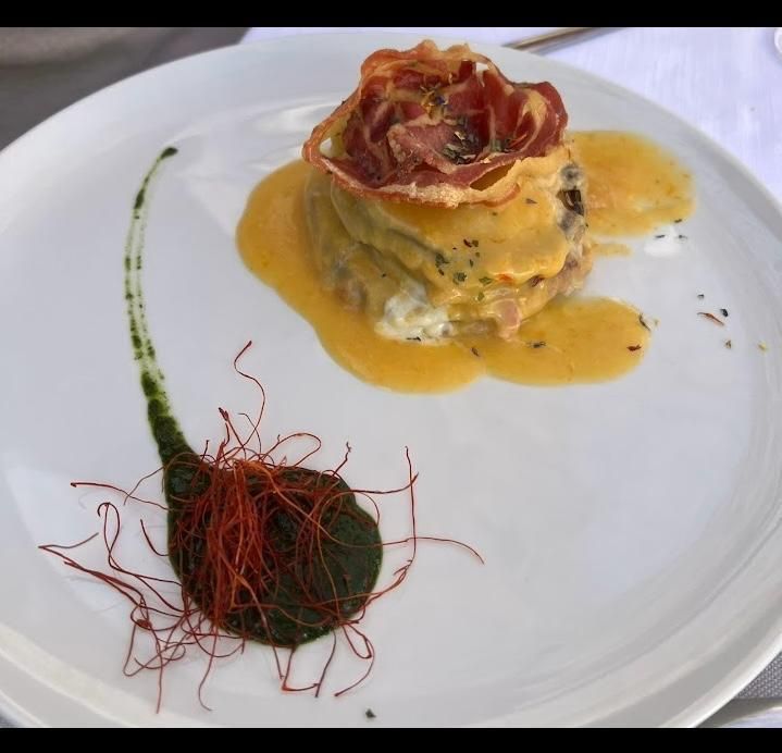 Piatto bianco con una pietanza gourmet servita in salsa gialla e guarnita con un verde decorato con sottili fili rossi.